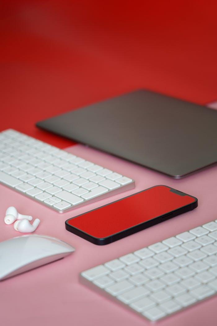services-04 Stylish flat lay of modern gadgets including a smartphone, keyboard, and mouse on a red background.