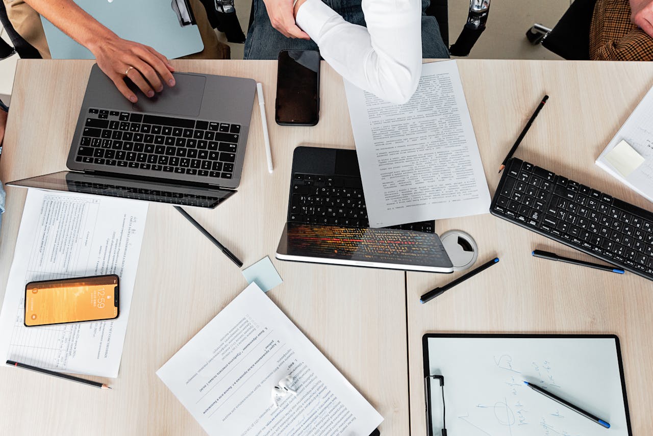 about-us Overhead shot of office desk with laptops, documents, and tech gadgets during a business meeting.